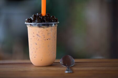 Ice bubble milk tea in takeaway glass on wooden plate - blurry backgroundの写真素材