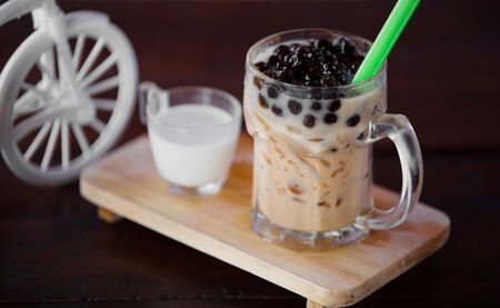 Ice bubble milk tea in takeaway glass on wooden plate - blurry backgroundの写真素材