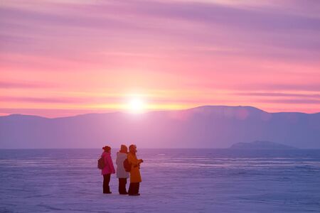 Winter sunset sun surrounded by ice and three backpackersの写真素材