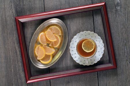 tea with lemon and marmalade in a frame on a wooden tableの写真素材