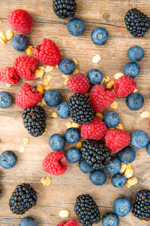 Close-up on blackberries, blueberries, raspberries and granola, top view flat lay on a wooden table