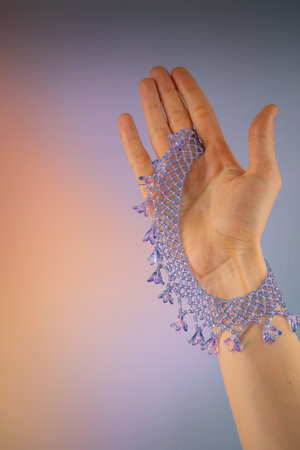 Hand holding lilac and pink bracelet made of beads on multicolored backgroundの写真素材