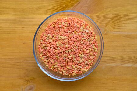 Red lentils in a glass bowl on yellow wooden table.
