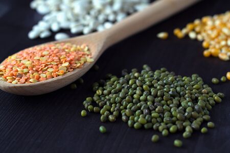 close-up green mung on wooden table with red and yellow lentils in wooden spoon on a black...