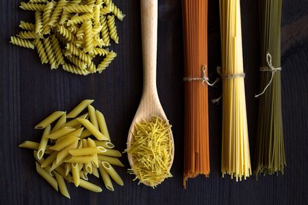 spaghetti and pasta on a wooden table. top view. uncooked wheat, Tomato and Spinach spaghetti and fusilli, penne on a dark background. Italian Cuisineの写真素材
