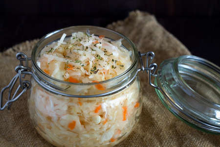 close-up homemade sauerkraut with carrots with herbs in glass jar on a black background. Pickled...