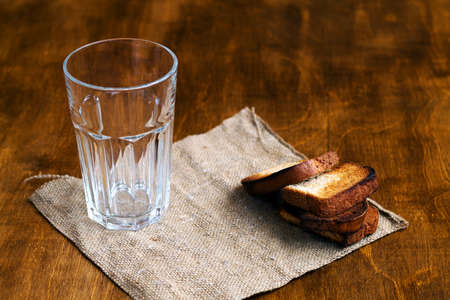 empty glass with black rye bread and hard chucks on a wooden table. glass with sackcloth on brown background.の写真素材