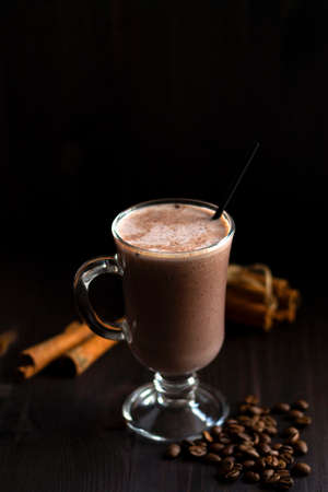 cup of cacao. glass of hot chocolate with whipped cream, coffee beans and cinnamon sticks on a dark background. hot drinks on a wooden background. winter and autumn. vertical. copy spaceの写真素材