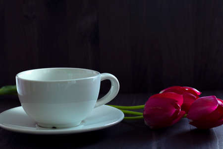 cup of coffee.still life with red tulips. bouquet of tulips with white coffee cup. Bright spring tulips flowers on black background. Copy space. red tulips on black table. Selective focus.の写真素材
