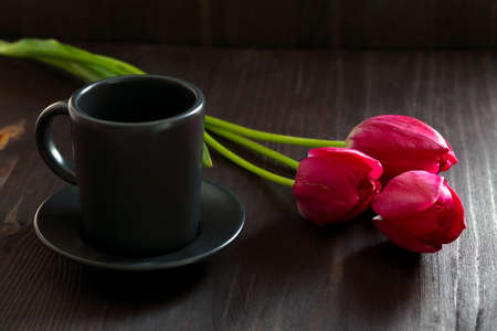 bouquet of tulips with black coffee cup. Bright spring tulips flowers on black background. Copy space. red tulips on black table. top view.の写真素材