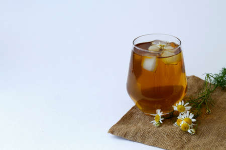 chamomile tea on sackcloth. glass cup of iced Herbal chamomile tea on a white table with copy space. cup of tea with fresh flowers and green leaves on white background.の写真素材