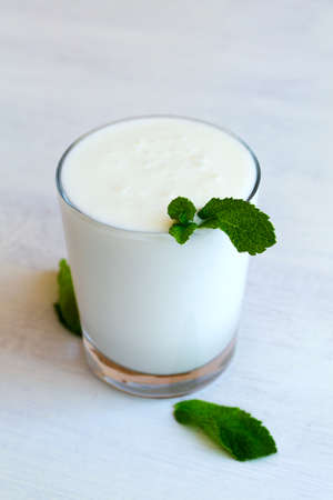glass of cold dairy Lassi drink with fresh green mint on white background. healthy, fermented products concept. Copy space. Kefir, yogurt or milk with probiotics on the table. Indian cuisine. verticalの写真素材