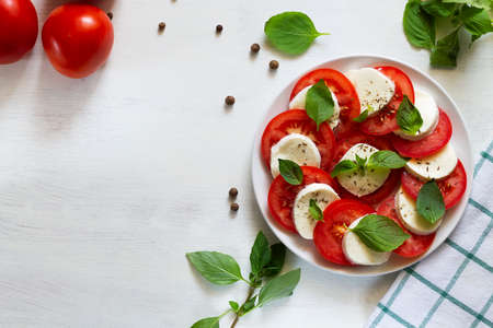 tomato salad with basil sliced tomatoes, mozzarella, green basil, olive oil on a white...