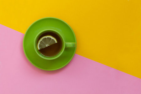 green tea cup on table.top view of green cup saucer with black tea with lemon or coffee on the color background with yellow and pink copy space.の写真素材