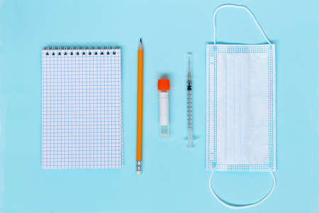 back to school.syringe with liquid, ampoules with medication, pen with notebook and medical face masks for children on the blue background. concept save life covid-19 top view. copy space. vaccinationの写真素材