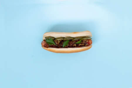 danish Hot dog with different toppings: pickles, fried onion, tomatoes with green on a light blue background with copy space. Fast food concept.の写真素材