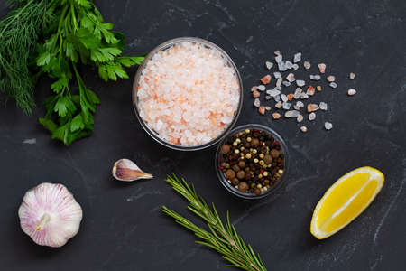 Set of various spices for cooking. fresh garlic, yellow lemon, greens, Pink Himalayan salt and mix of peppers in a glasses bowls on the black background. Top view copy space.の写真素材