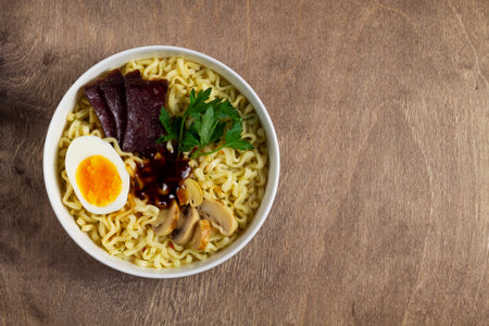 Traditional Asian cuisine. A white bowl of Korean soup with food sticks on the brown. ramen noodles with chicken, boiled egg, mushrooms, spring onions and soy sauce. top view.の写真素材