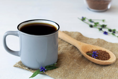 coffee substitute. Gray Cup of delicious chicory drink with Ground chicory root on a wooden spoon and blue chicory flowers on white table with sackcloth. hot and healthy drinks.の写真素材