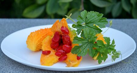 Ripe and sweet, orange momordica with green leaves on a white plateの写真素材