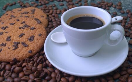 Fragrant black coffee in a white cup and saucer. Sprinkled coffee beans. Perfect cookies with chocolate chips.の写真素材