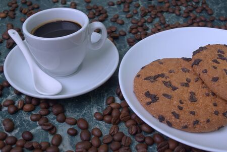 Fragrant black coffee in a white cup and saucer. Sprinkled coffee beans. Perfect cookies with chocolate chips.の写真素材