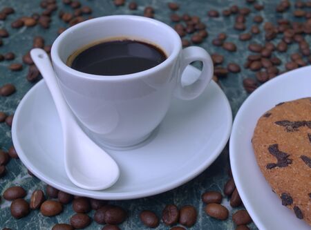 Fragrant black coffee in a white cup and saucer. Sprinkled coffee beans. Perfect cookies with chocolate chips.の写真素材