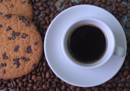Fragrant black coffee in a white cup and saucer. Sprinkled coffee beans. Perfect cookies with chocolate chips.の写真素材