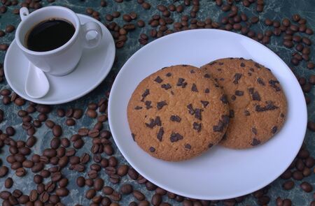 Fragrant black coffee in a white cup and saucer. Sprinkled coffee beans. Perfect cookies with chocolate chips.の写真素材