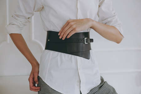 Young girl in a white office shirt trying on a leather beltの写真素材