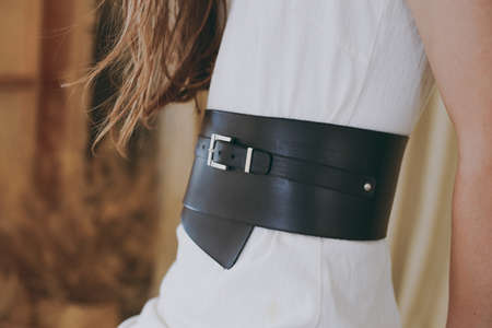 A slim girl in a white dress tries on a belt with black leatherの写真素材