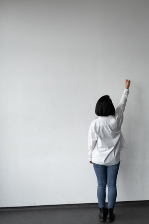 Woman in white shirt with short haircut, writer, writing on the wall, vertical photo for advertisingの写真素材