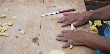 Knead the homemade orecchiette baresi. Typical fresh pasta from Bari, Puglia region, Italy. Working hands. Hands of an old woman. Italian small business owners. Ancient tradition.の写真素材