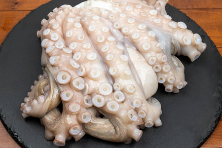Fresh octopus on black slate plate on wooden table, close up