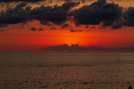 he blood-red sky over the surface of the sea, lit by the setting sun hidden behind the dark cloudsの写真素材