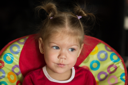 portrait of little girl with pensive look sitting in feeding chair looking asideの写真素材