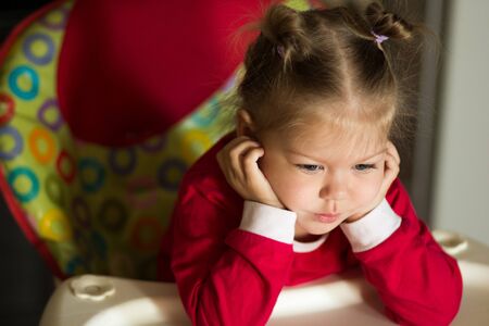 portrait of thinking and sad little girl propping head by hands looking down