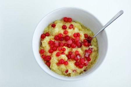 Homemade healthy maize porridge with frozen red currant in white bowl on the white tableの写真素材
