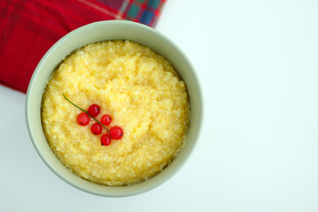 View from above of maize porridge in bowl with branch red currant on it served with red napkin on white tableの写真素材