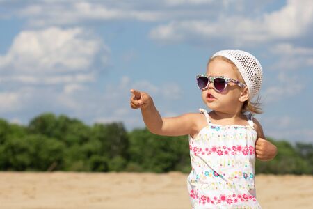 Little girl in sunglasses pointing finger hand aside and looking asideの写真素材