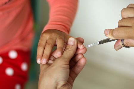 Womans hand holding kids hand cut toddler fingernail with manicure scissorsの写真素材
