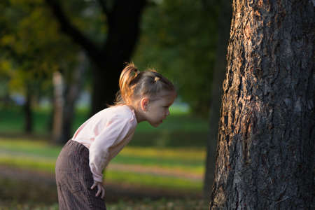 Little girl looking at tree attentively and studying something on itの写真素材