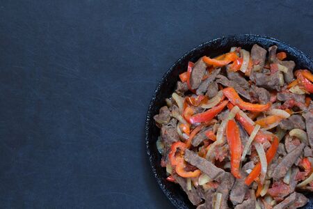 Top view of cooked liver with vegetables on frying pan on the black backgroundの写真素材