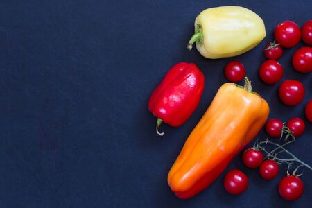 Colorful fresh peppers and tomatoes cherry on the black backgroundの写真素材