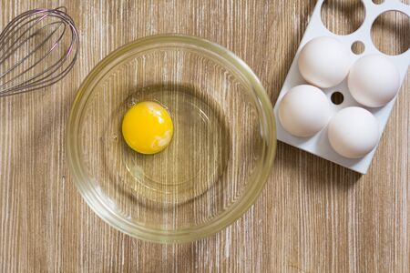 One raw chicken yolk and whites in glass bowl on the wooden tableの写真素材