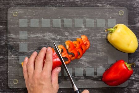 Hand of woman cutting fresh pepper with knife on the glass cut board on the black backgroundの写真素材