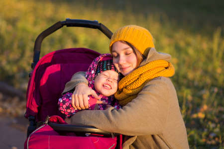 Young woman and little girl hugging each other in the autumn park