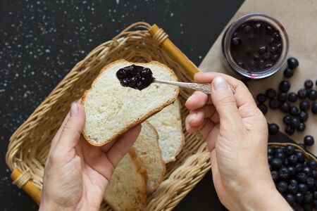 Top view of woman hand putting chokeberry jam on toast