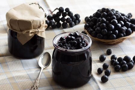 Chokeberry jam in jar and chokeberries on tableの写真素材