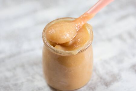 Apple sauce in glass jar and spoon on white background